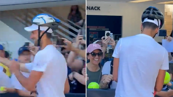 Novak Djokovic greets fans wearing a helmet after getting hit on head with water bottle