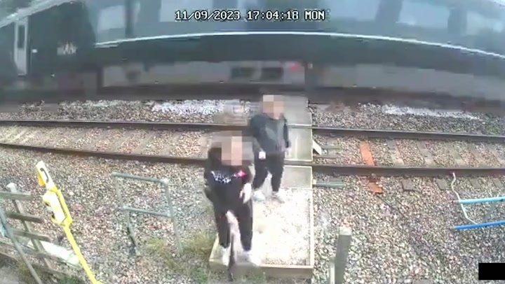 Children on level crossing push each other as train speeds past