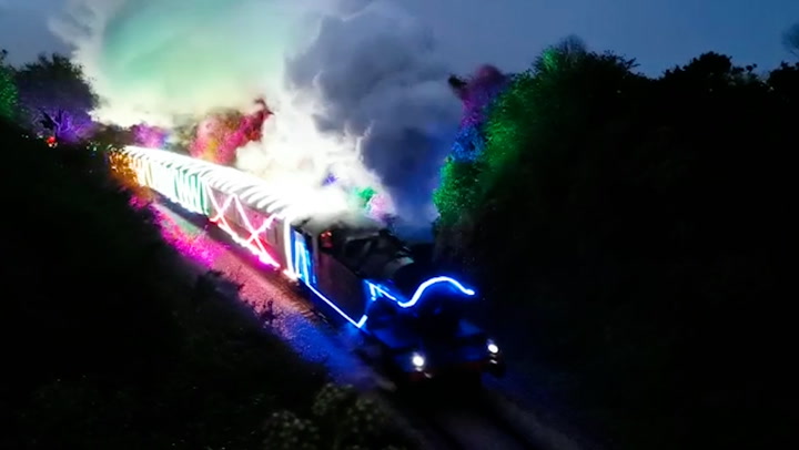 Steam train decked out in vibrant neon lights passes through countryside