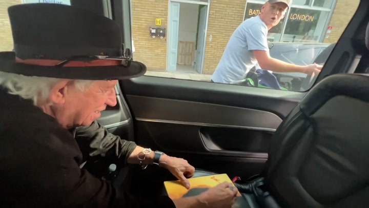 Keith Richards jokes with cyclists as he signs autograph for him in back of taxi