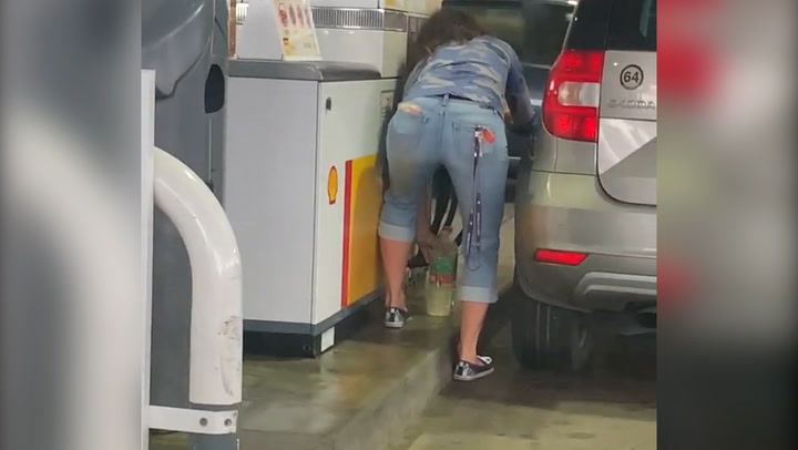 Woman empties water bottles and fills them with petrol at pump
