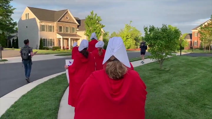 Pro-choice protestors in Handmaids' Tale costumes surround Justice's house