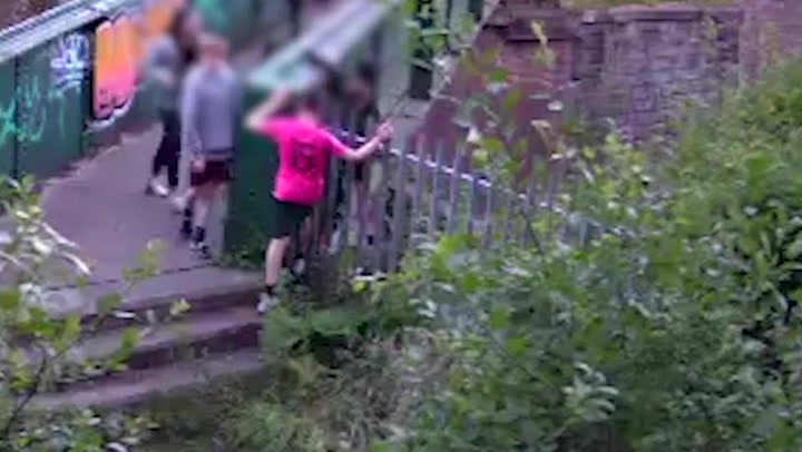 Group of children dangle from ledge of bridge above train tracks