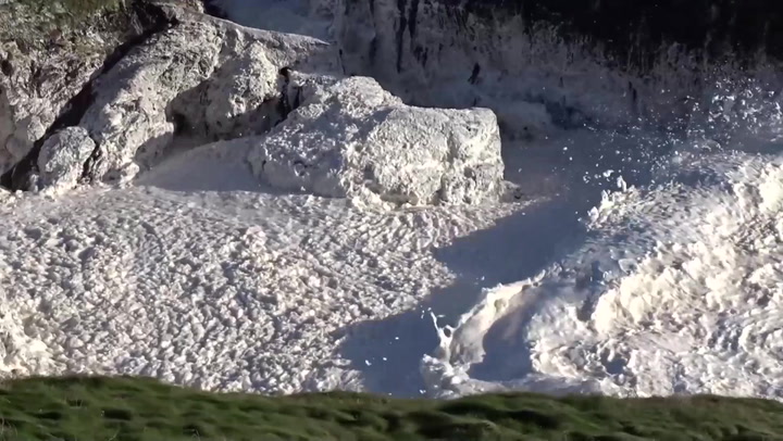 Waves of sea foam wash up at Cornish cove