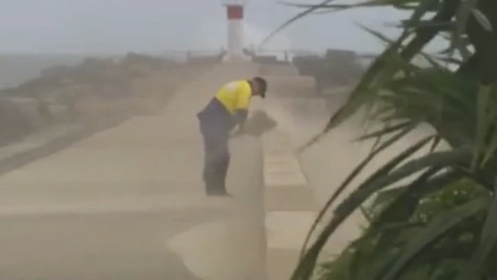 Determined beach worker continues to shovel sand during 65km/h winds