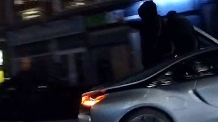 Driver speeds down Oxford road with two men on sat on sports car roof